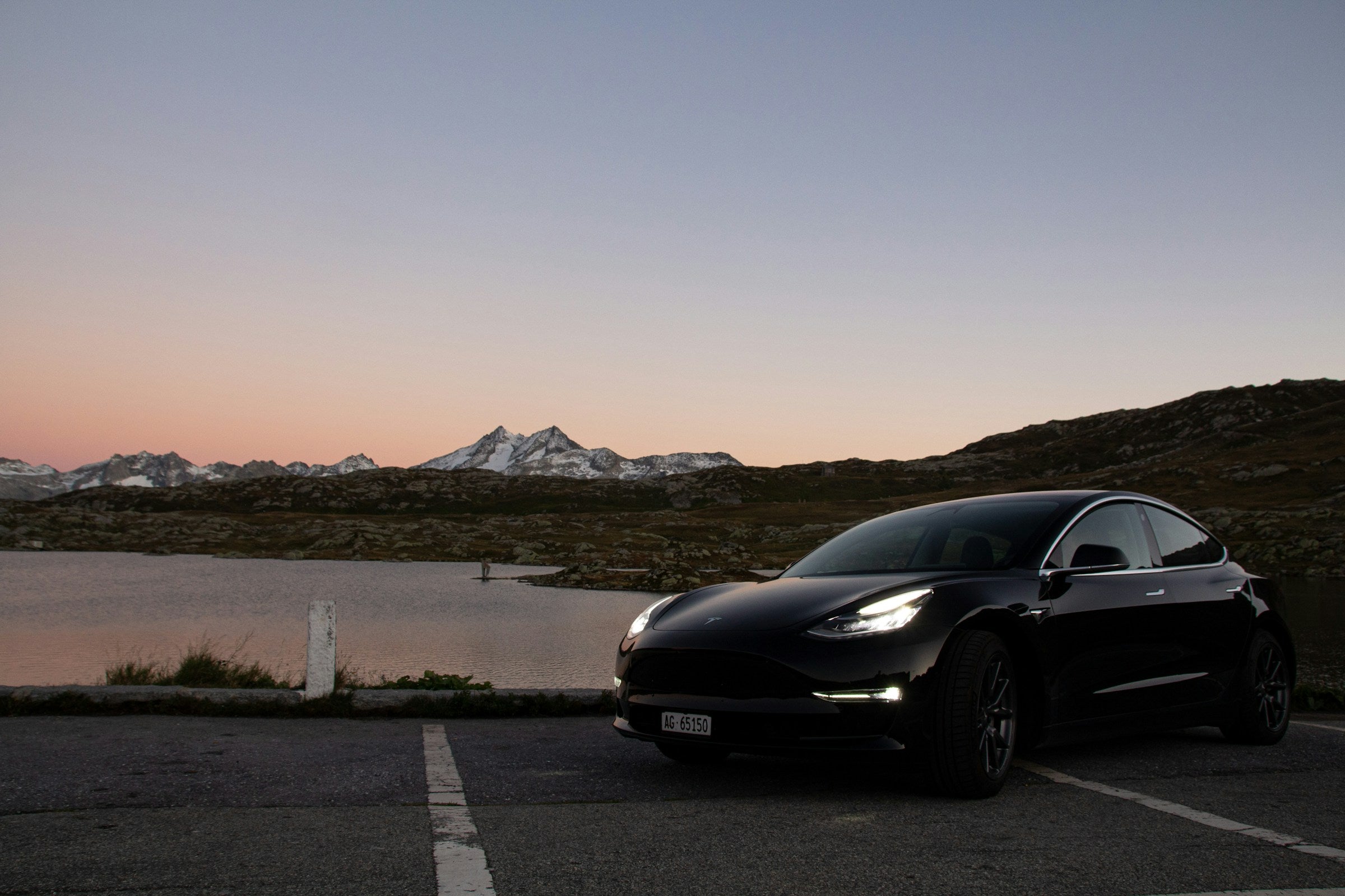 Tesla Model 3 junto a un lago entre montañas